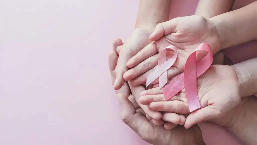 Volunteers standing with their hands stacked together, holding a breast cancer awareness badge